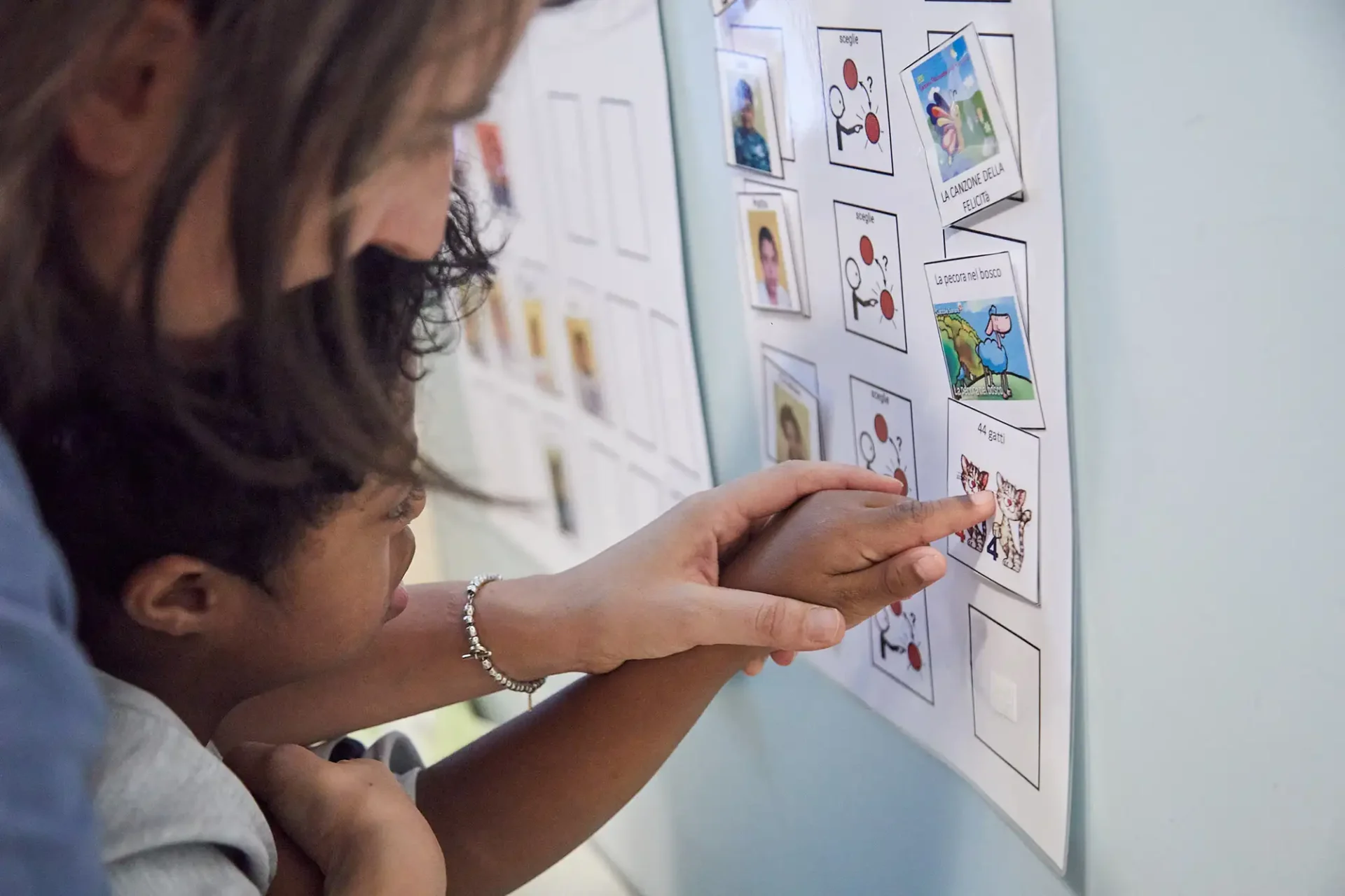 Un'operatrice di L'abilità supporta un bambino nella lettura di una scheda con i simboli in CAA.