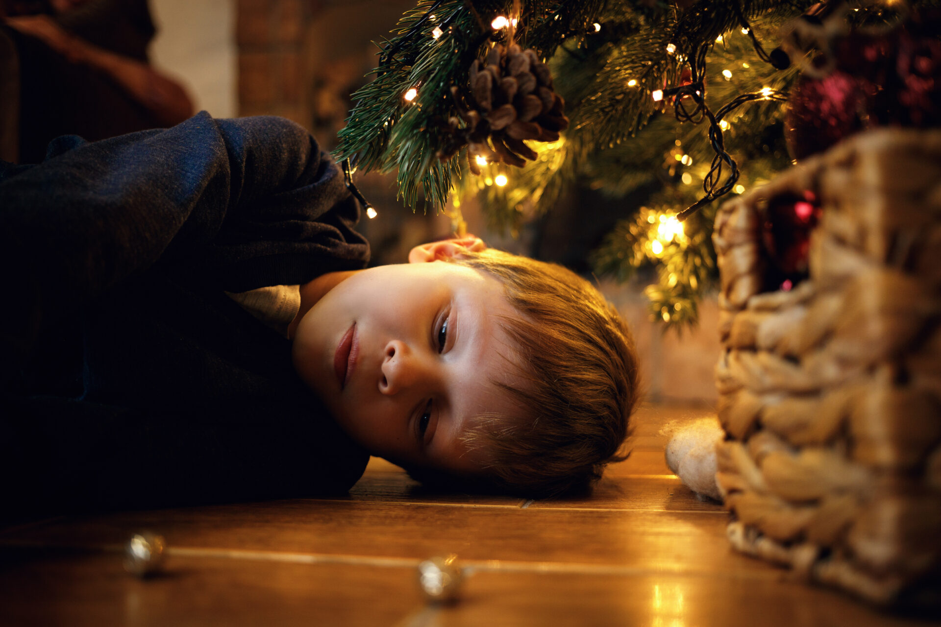 In questa foto, un bambino con gli occhi chiusi è disteso per terra. Sullo sfondo, si vede un albero di Natale