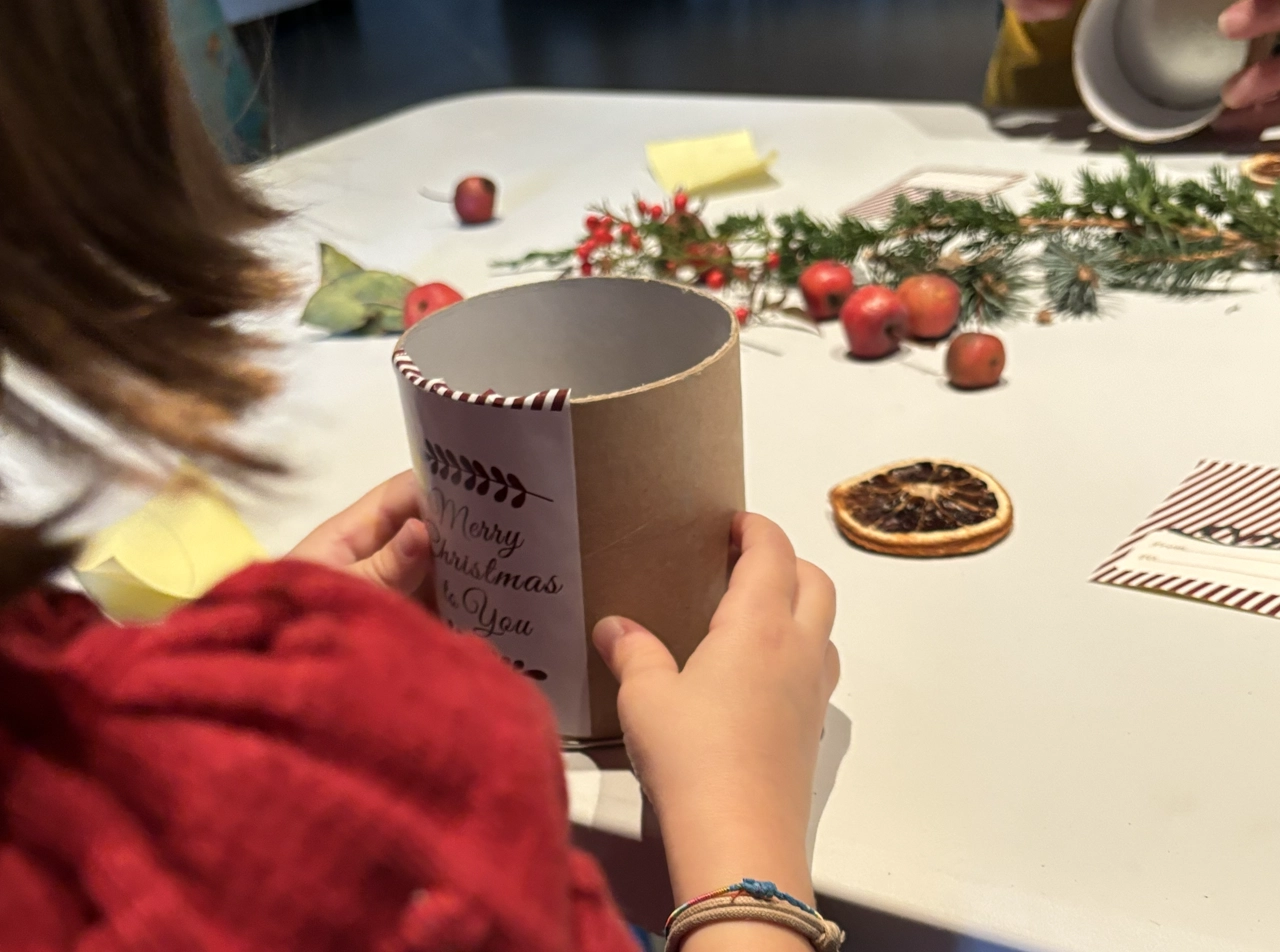 In questa foto si vedono le mani di una bambina che tiene in mano del materiale per fare un centrotavola natalizio.