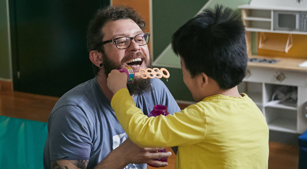 In questa foto si vede un bambino di La Casa di L'abilità che gioca con le bolle di sapone insieme a un operatore.